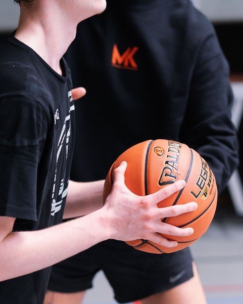 A basketball ball holded by a pair of hands. The torso of Michael Krikemans in the background.